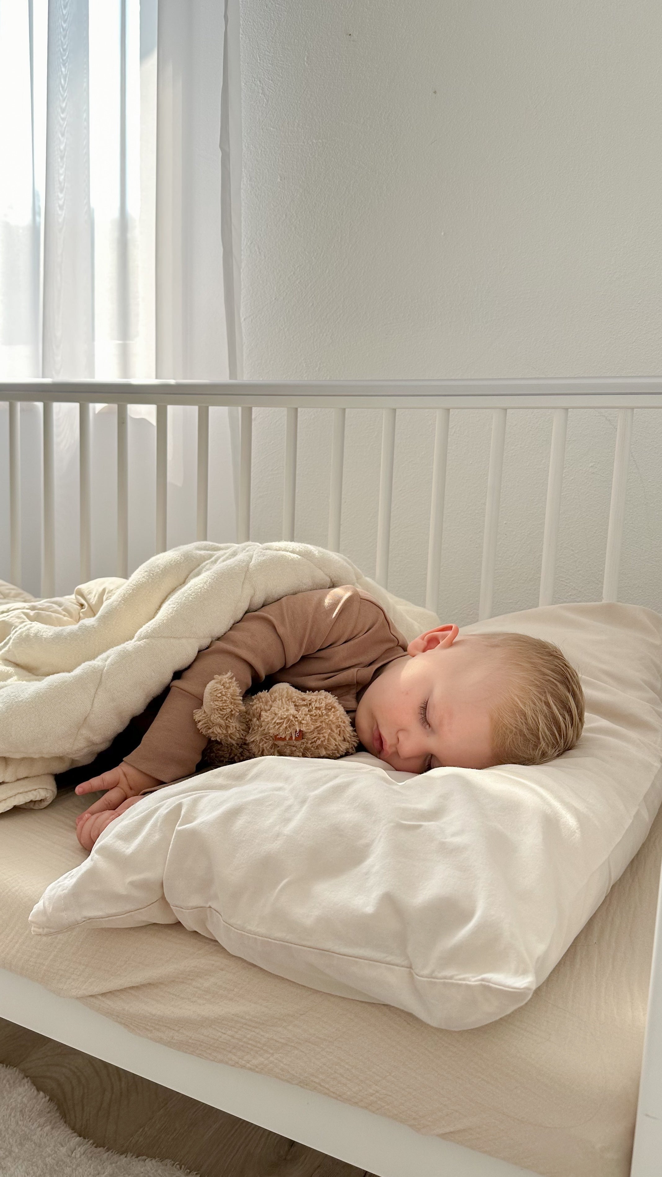 Schlafendes Baby in mitwachsendem, veganem Biobaumwoll-Schlafanzug in neutralen Tönen im weißen Babybett mit Kuscheltier