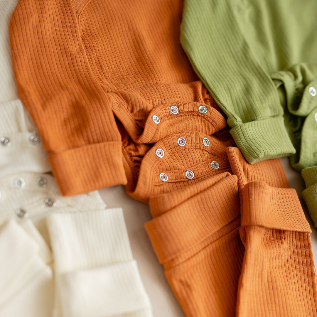 Nahaufnahme von mitwachsenden, veganen und GOTS-zertifizierten Babybodys in Orange, Grün und Creme mit Druckknöpfen