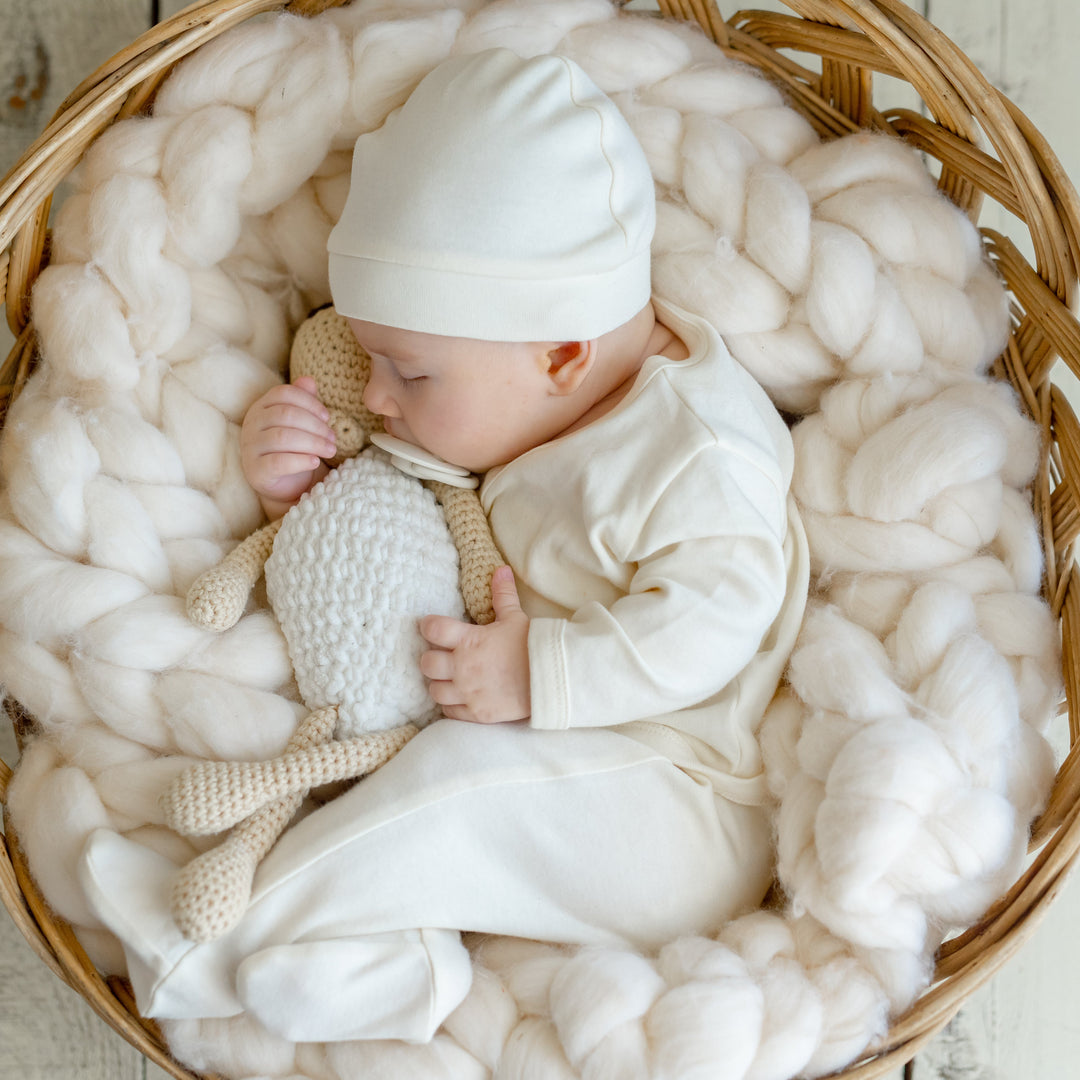 Schlafendes Baby in Bio-Babymode aus Biobaumwolle, umgeben von weicher Kuscheldecke und Rattankorb